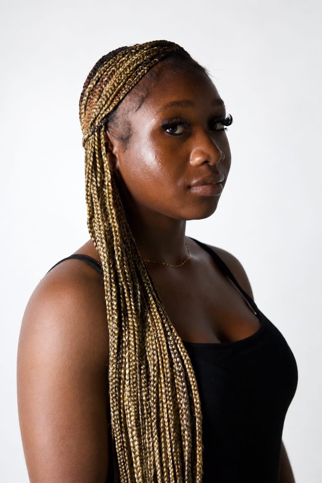 Adwoa looks back over her bare shoulder, long golden braids falling across a black camisole